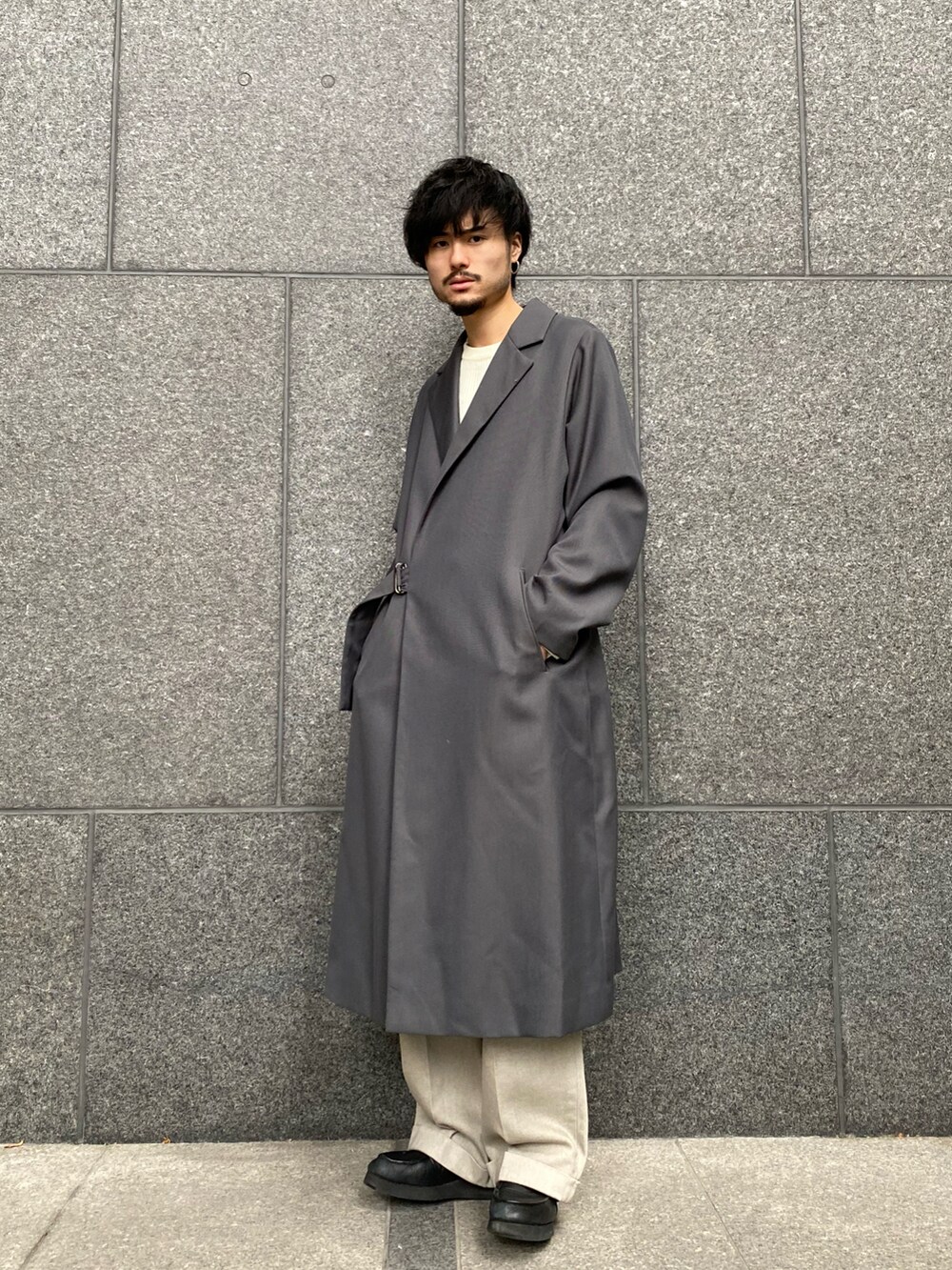 グレー系のトレンチコート、ベージュ系のデニムパンツ、ホワイト系のニット/セーターを着用したメンズの秋コーディネートの2枚目の写真