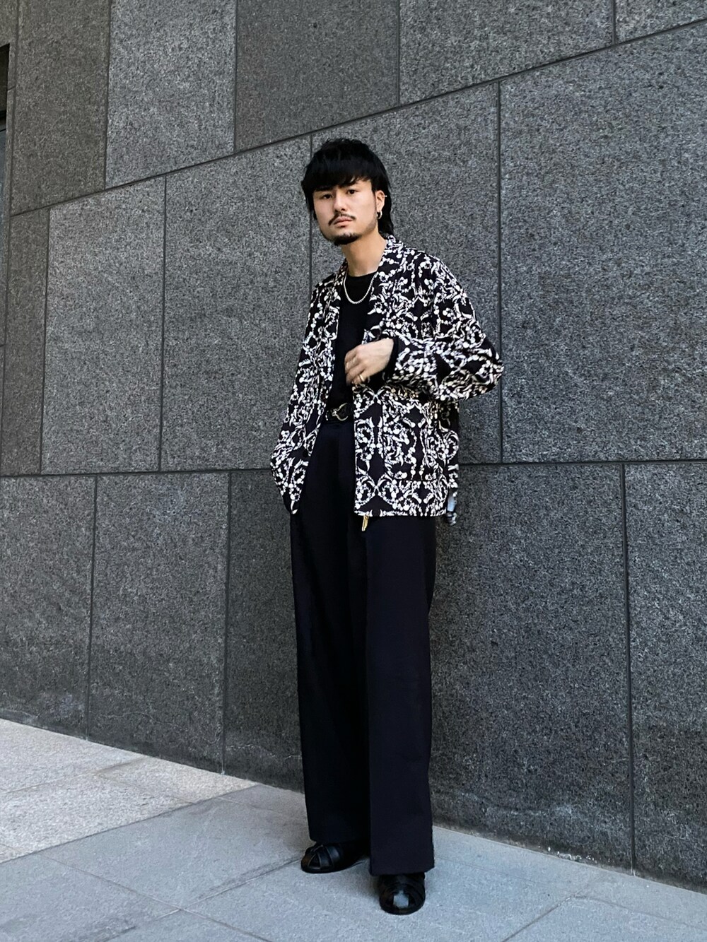 ブラック系のテーラードジャケット、ブラック系のスラックス、ブラック系のサンダルを着用したメンズの春コーディネートの2枚目の写真