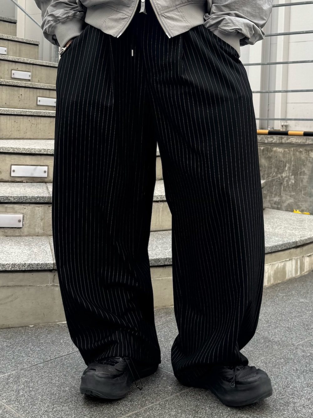 グレー系のMA-1、ブラック系のスラックスを着用したメンズの春コーディネートの6枚目の写真