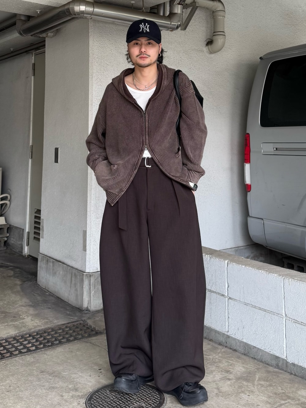 ブラウン系のパーカー、グレー系のスラックス、ブラック系のショルダーバッグを着用したメンズの春コーディネートの2枚目の写真