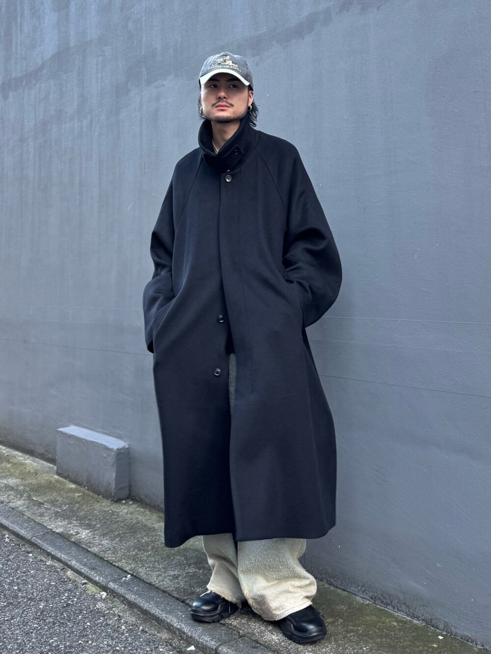 ブルー系のニット/セーター、ブルー系のデニムパンツ、ブラック系のステンカラーコートを着用したメンズの秋コーディネートの4枚目の写真