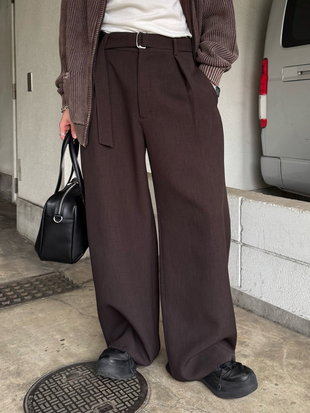 ブラウン系のパーカー、グレー系のスラックス、ブラック系のショルダーバッグを着用したメンズの春コーディネートの9枚目の写真