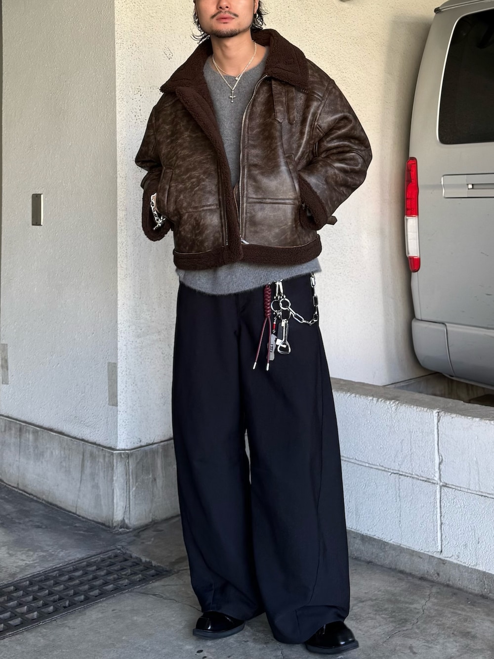 ブラック系のスラックス、グレー系のニット/セーター、ブラウン系のブルゾンを着用したメンズの秋コーディネートの3枚目の写真