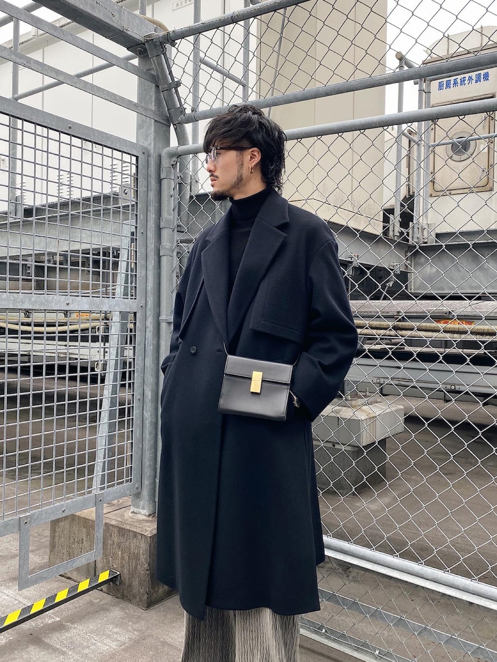 ブラック系のチェスターコート、ブラック系のショルダーバッグ、グレー系のスラックスを着用したメンズの冬コーディネートの4枚目の写真