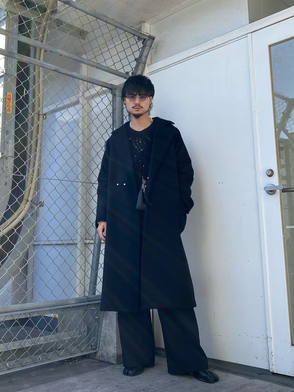 ブラック系のチェスターコート、ブラック系のニット/セーター、ブラック系のスラックスを着用したメンズの冬コーディネートの2枚目の写真