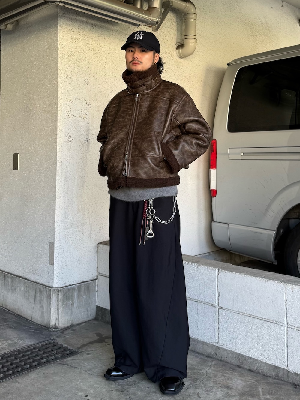 ブラック系のスラックス、グレー系のニット/セーター、ブラウン系のブルゾンを着用したメンズの秋コーディネートの2枚目の写真