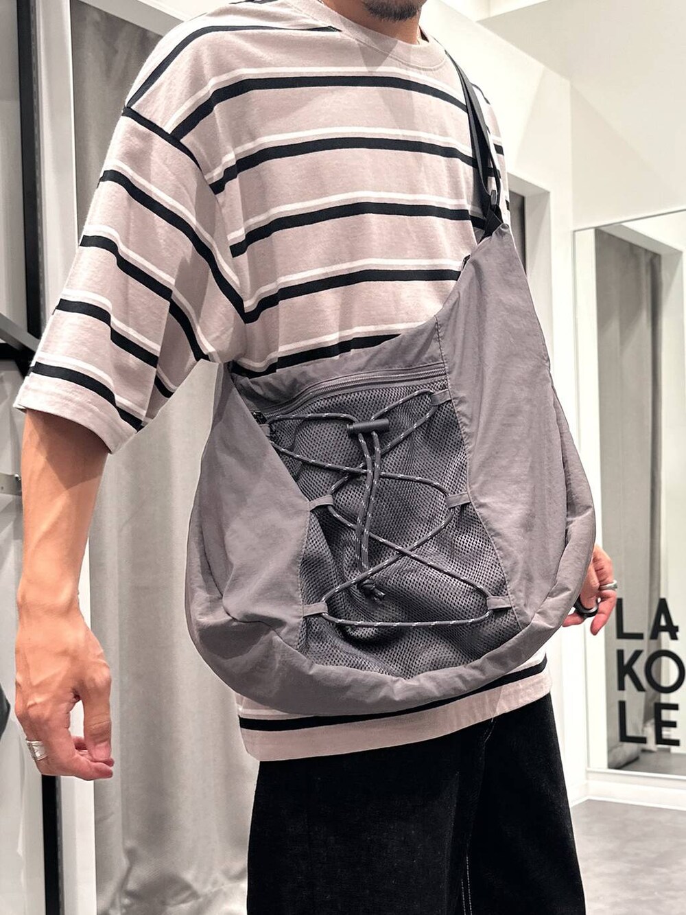 ブラック系のデニムパンツ、ベージュ系のTシャツ/カットソー、グレー系のショルダーバッグを着用したメンズの夏コーディネートの5枚目の写真