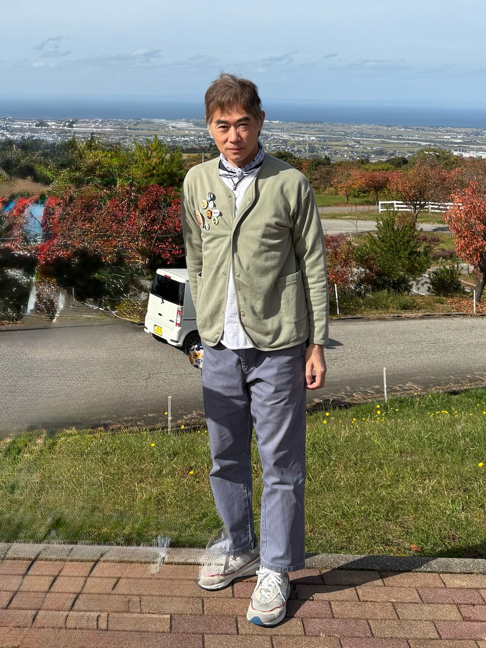 グリーン系のカーディガン/ボレロ、ホワイト系のスニーカー、ブルー系のチノパンツを着用したメンズの秋コーディネートの2枚目の写真