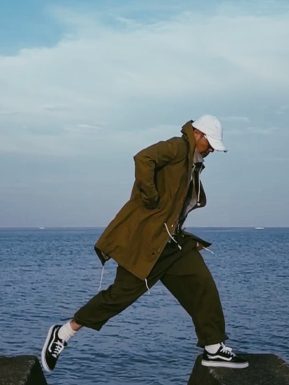 グリーン系のミリタリージャケット、ブラウン系のチノパンツ、ブラック系のスニーカーを着用したメンズの春コーディネートの2枚目の写真