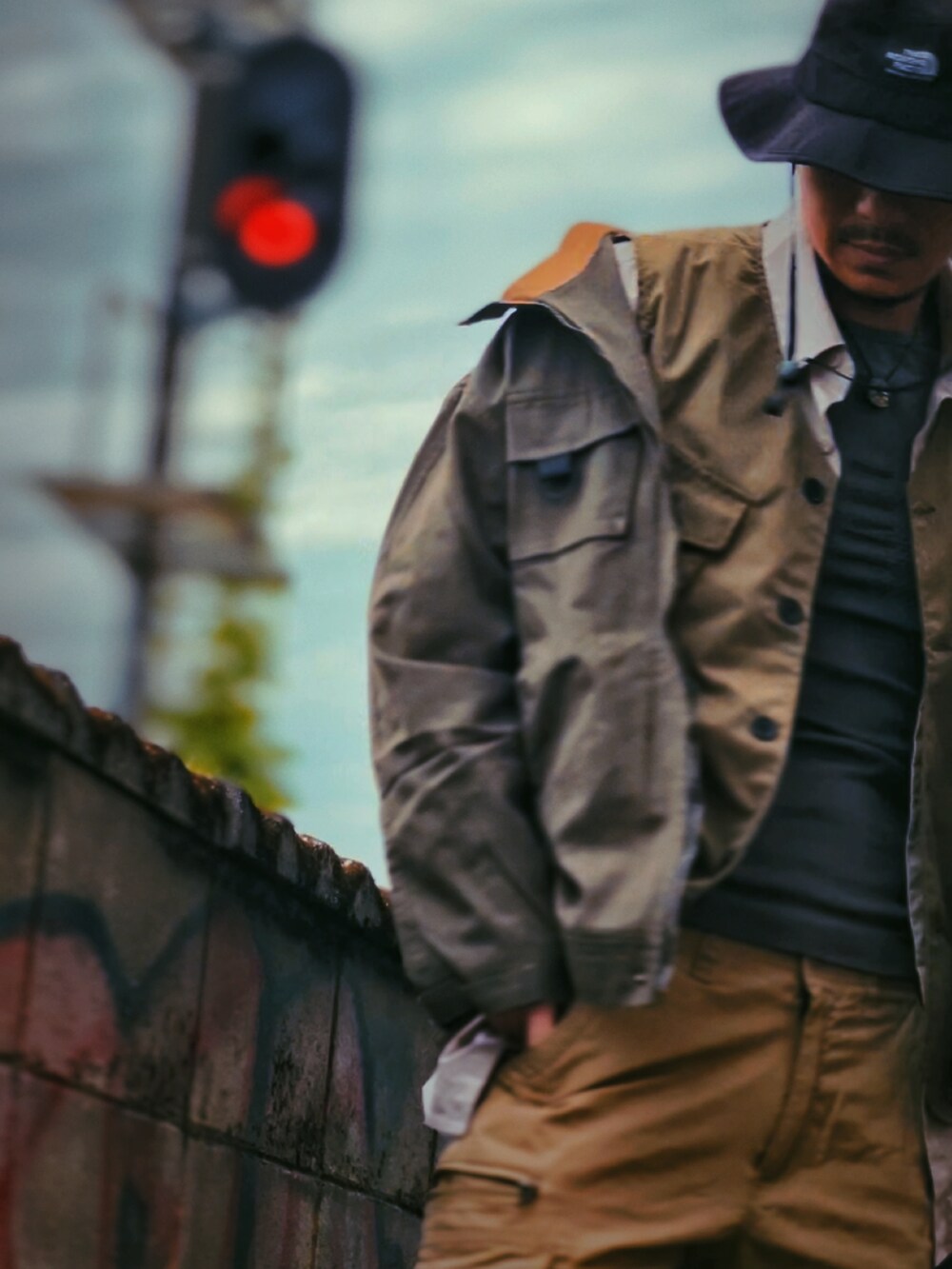 グリーン系のミリタリージャケット、ベージュ系のベスト、ベージュ系のカーゴパンツを着用したメンズの春コーディネートの3枚目の写真