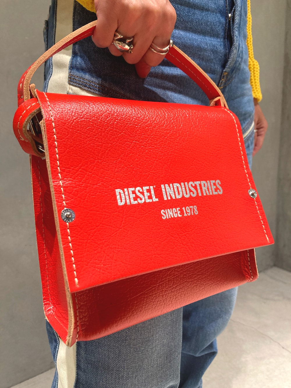 レッド系のショルダーバッグ、ブルー系のデニムパンツ、イエロー系のニット/セーターを着用したレディースの夏コーディネートの2枚目の写真