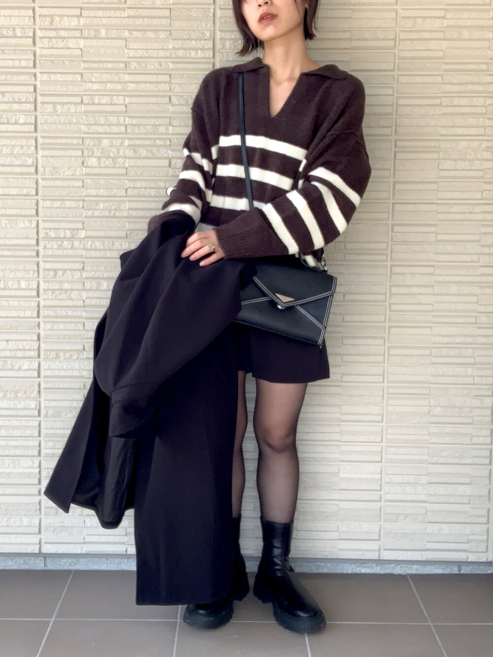 ブラック系のステンカラーコート、ブラック系のその他パンツ、ブラウン系のニット/セーターを着用したレディースの冬コーディネートの2枚目の写真