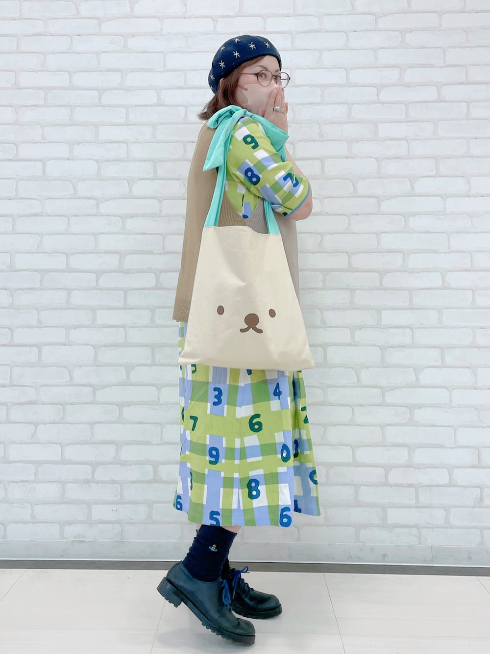 ベージュ系のベスト、グリーン系のトートバッグ、グリーン系のワンピース/ドレスを着用したレディースの秋コーディネートの2枚目の写真