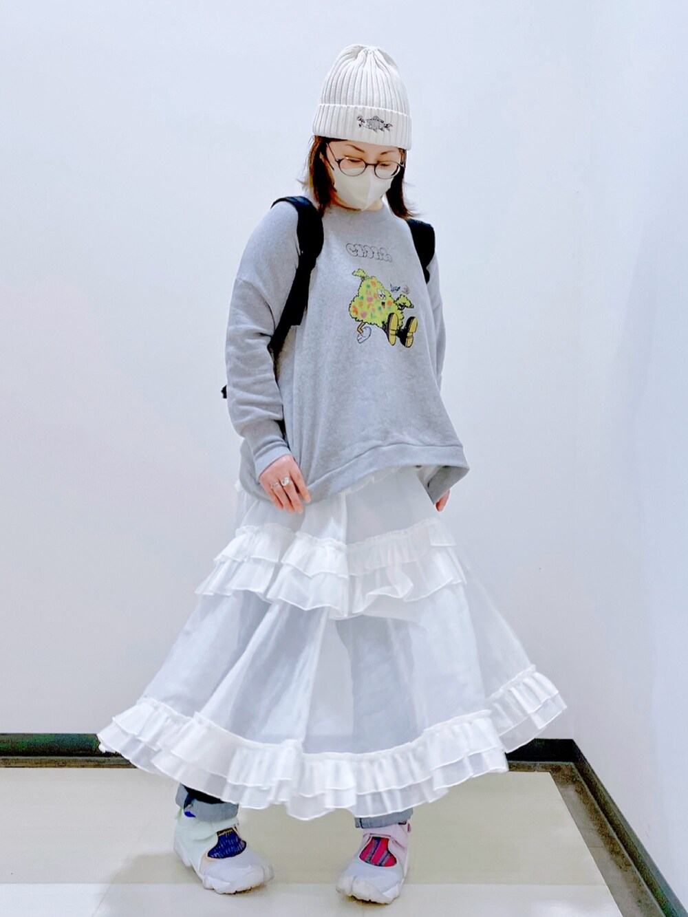 グレー系のスウェット、ホワイト系のスカート、ブルー系のデニムパンツを着用したレディースの秋コーディネートの2枚目の写真