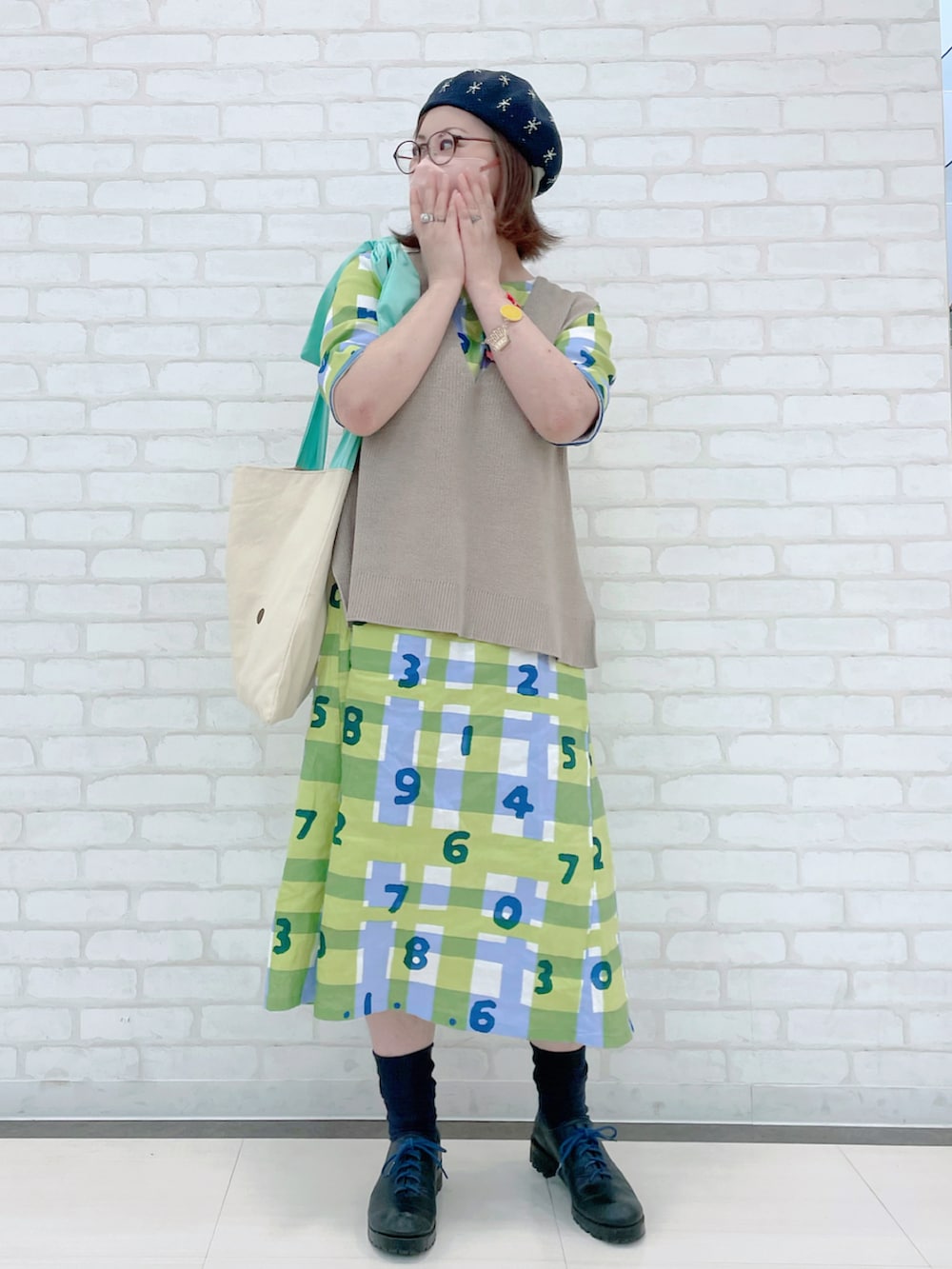 ベージュ系のベスト、グリーン系のトートバッグ、グリーン系のワンピース/ドレスを着用したレディースの秋コーディネートの3枚目の写真