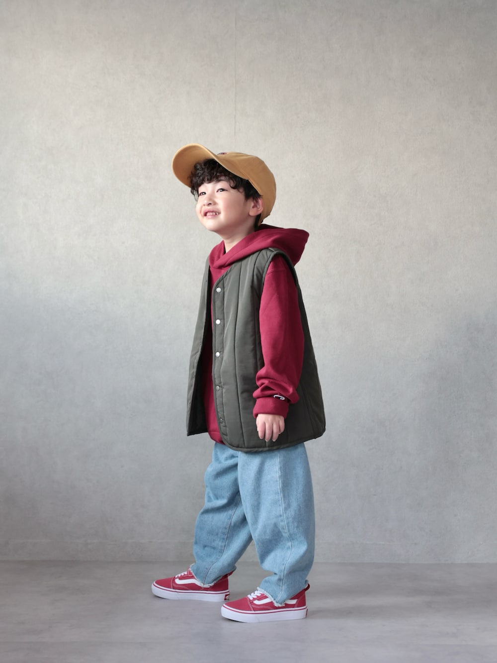 グリーン系のベスト、レッド系のパーカー、ブルー系のデニムパンツを着用したキッズの冬コーディネートの2枚目の写真