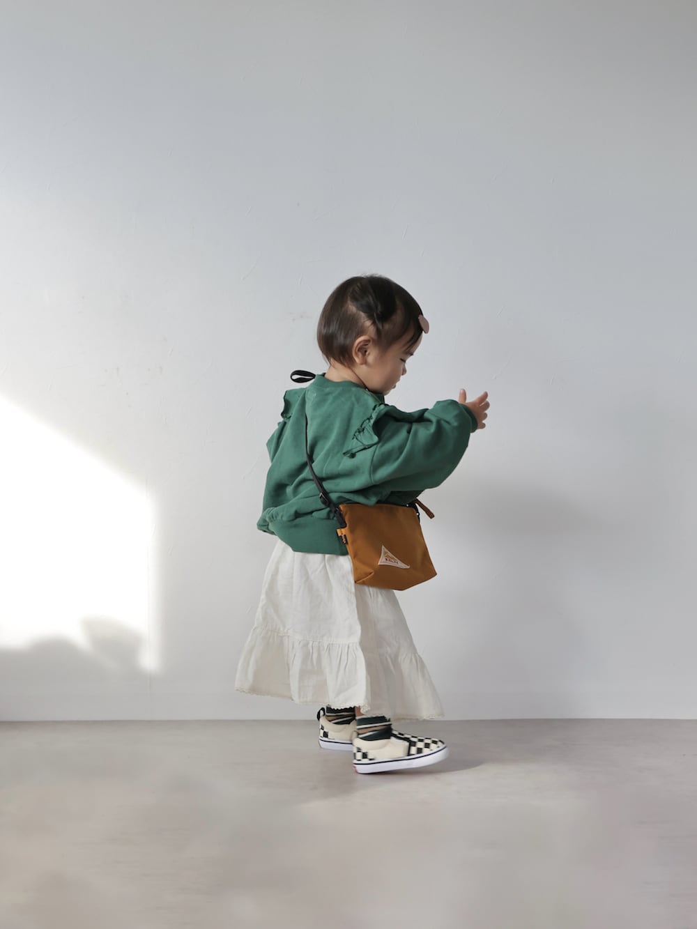 グリーン系のスウェット、ホワイト系のスカート、ブラウン系のショルダーバッグを着用したキッズの冬コーディネートの2枚目の写真
