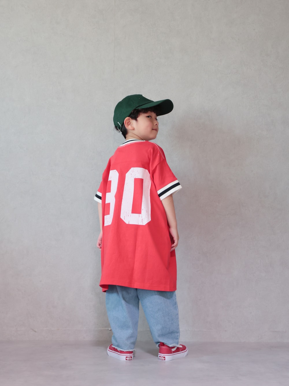 レッド系のワンピース、ブルー系のデニムパンツ、レッド系のスニーカーを着用したキッズの春コーディネートの3枚目の写真