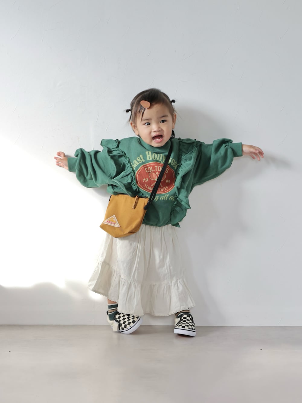 グリーン系のスウェット、ホワイト系のスカート、ブラウン系のショルダーバッグを着用したキッズの冬コーディネートの3枚目の写真