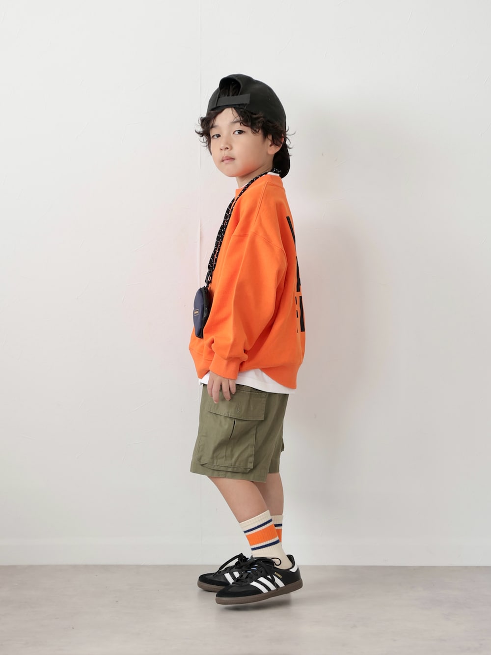 オレンジ系のスウェット、ブラック系のトップス、グリーン系のカーゴパンツを着用したキッズの秋コーディネートの4枚目の写真