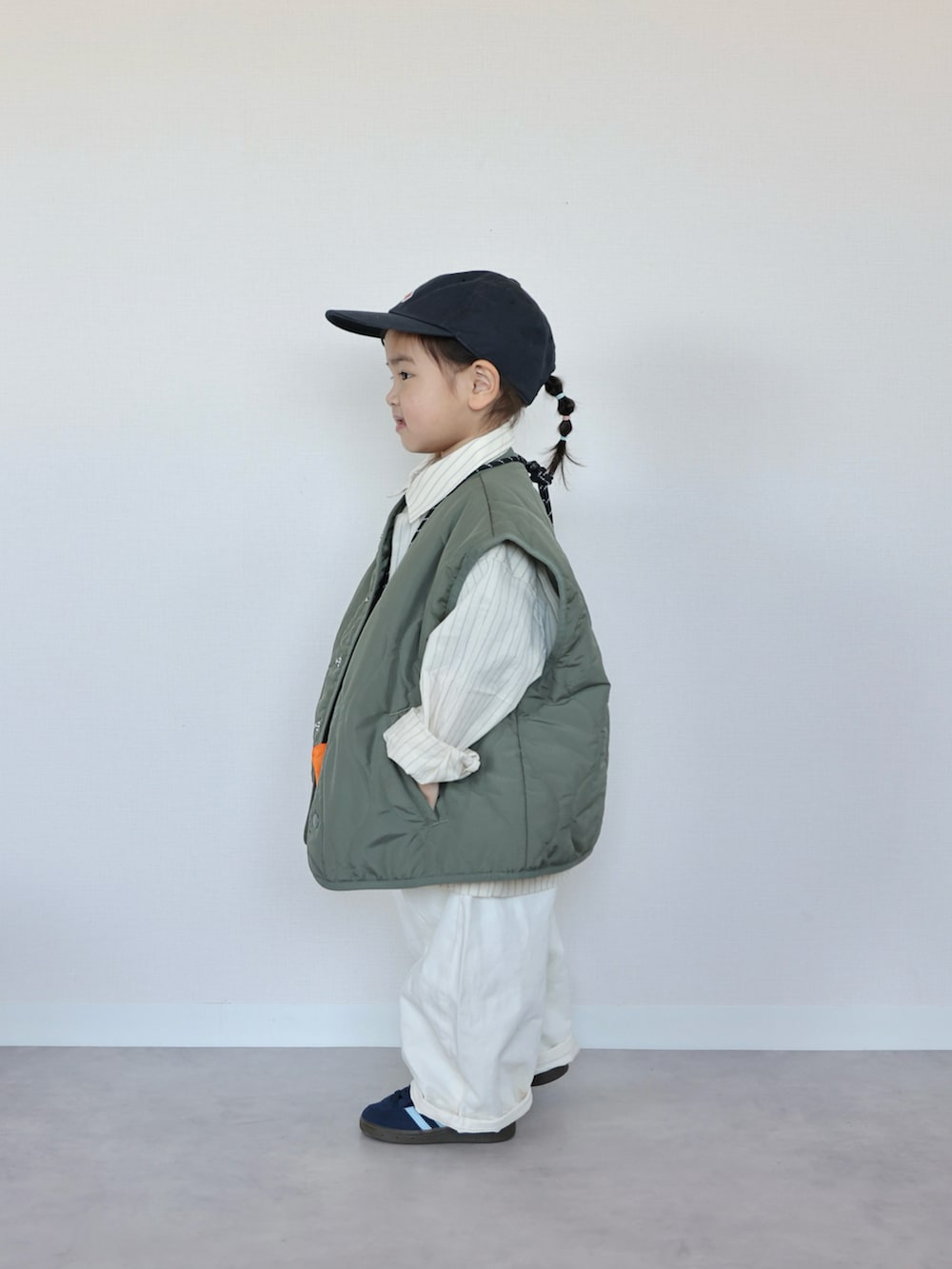 グリーン系のベスト、イエロー系のシャツ/ブラウス、ブルー系のスニーカーを着用したキッズの春コーディネートの2枚目の写真