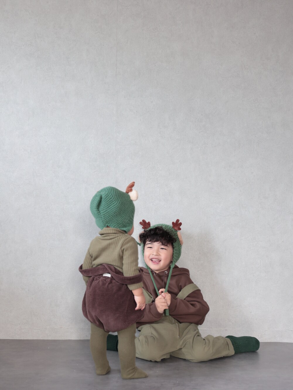 グリーン系のサロペット/オーバーオール、ブラウン系のパーカー、グリーン系のソックス/靴下を着用したキッズの冬コーディネートの3枚目の写真