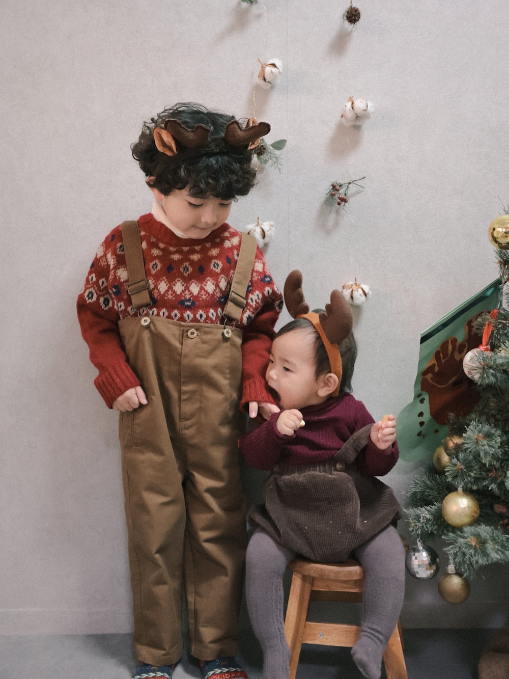 レッド系のニット/セーター、ホワイト系のTシャツ/カットソー、ブラウン系のサロペット/オーバーオールを着用したキッズの冬コーディネートの4枚目の写真