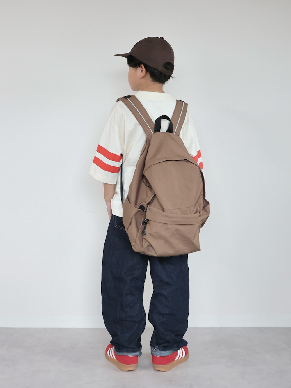 レッド系のスニーカー、ホワイト系のTシャツ/カットソー、ブラウン系のバックパック/リュックを着用したキッズの秋コーディネートの3枚目の写真