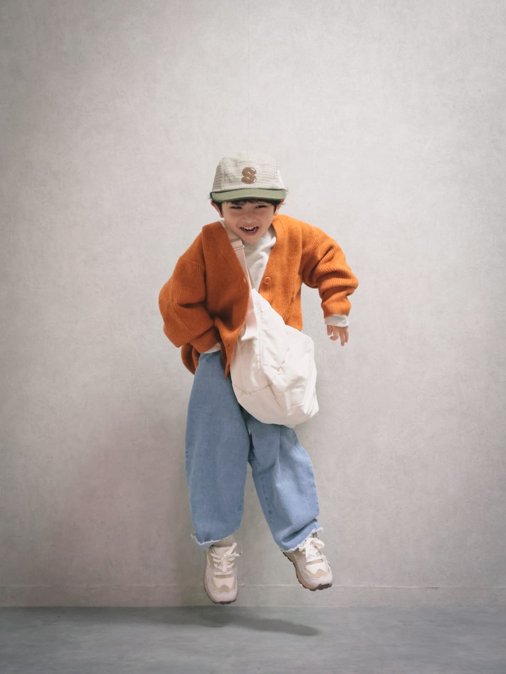 オレンジ系のニット/セーター、ホワイト系のスウェット、ブルー系のデニムパンツを着用したキッズの秋コーディネートの5枚目の写真