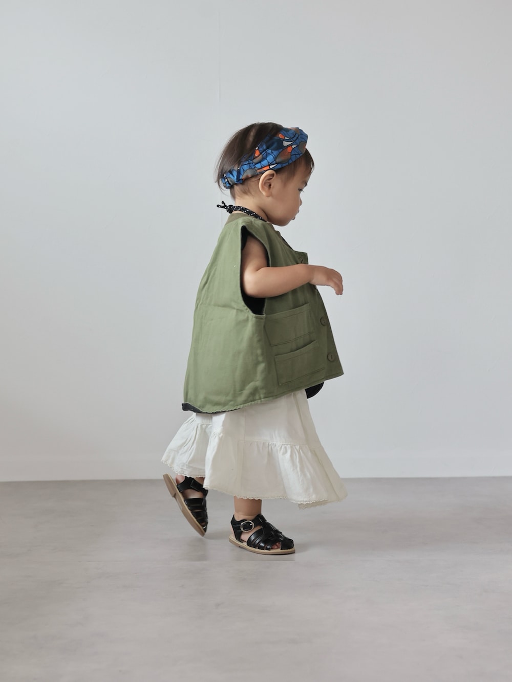 グリーン系のベスト、ブラック系のTシャツ/カットソー、ホワイト系のスカートを着用したキッズの夏コーディネートの2枚目の写真