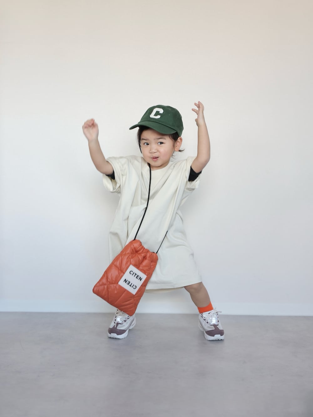 ホワイト系のTシャツ/カットソー、オレンジ系のショルダーバッグ、ホワイト系のスニーカーを着用したキッズの春コーディネートの3枚目の写真