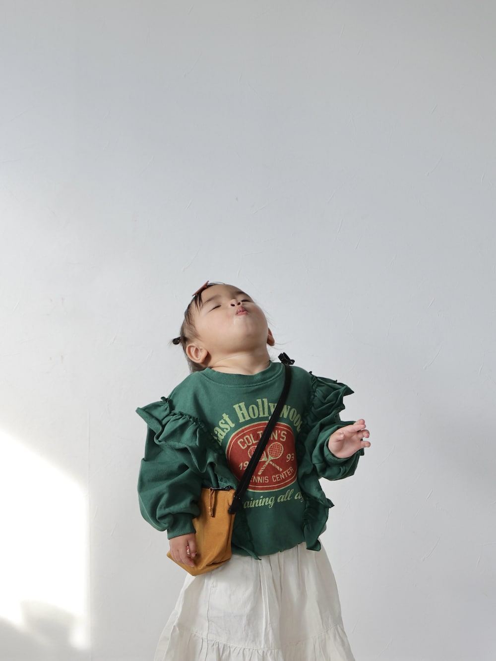 グリーン系のスウェット、ホワイト系のスカート、ブラウン系のショルダーバッグを着用したキッズの冬コーディネートの4枚目の写真