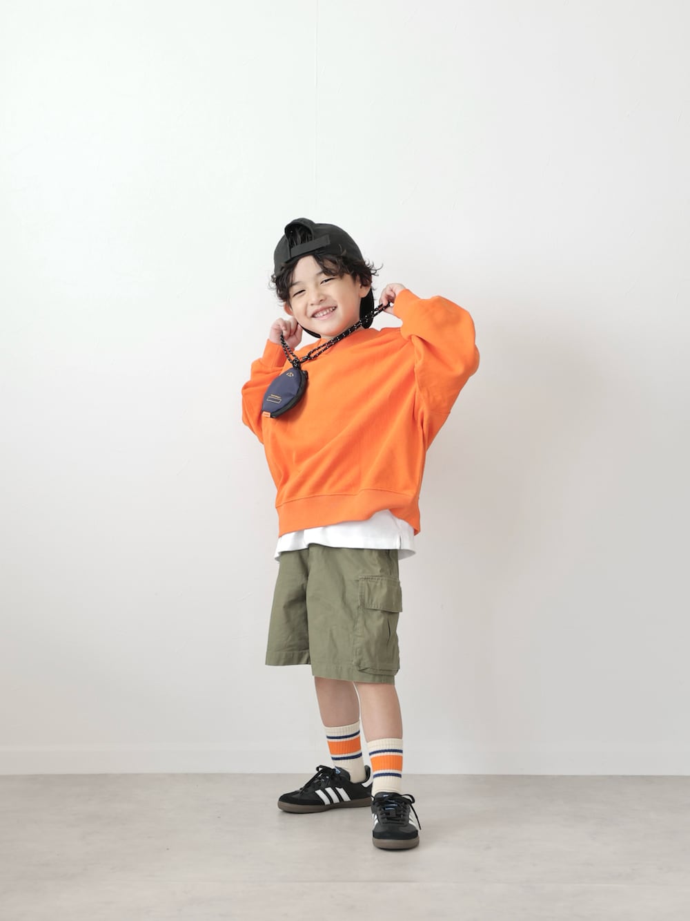 オレンジ系のスウェット、ブラック系のトップス、グリーン系のカーゴパンツを着用したキッズの秋コーディネートの5枚目の写真