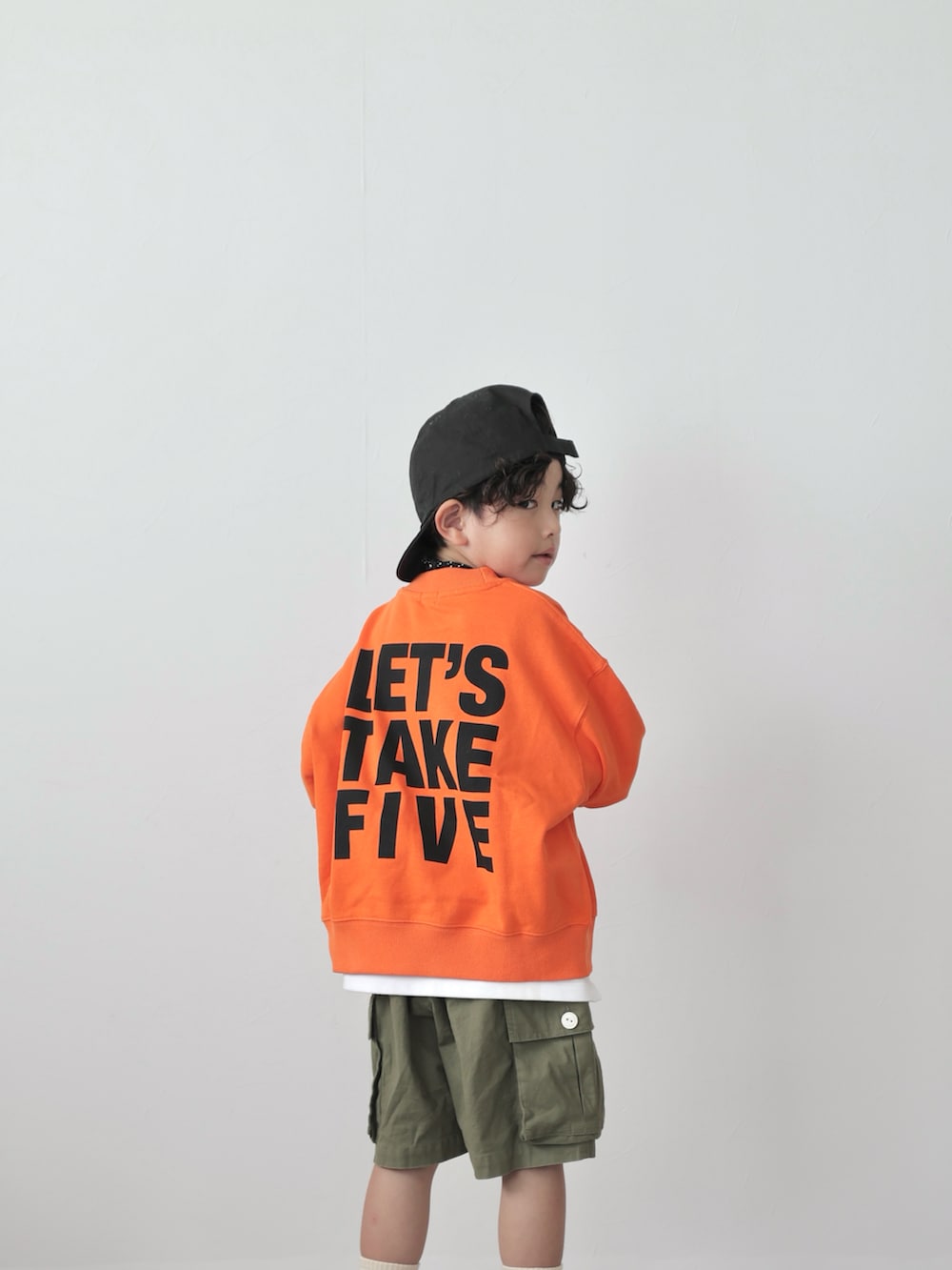 オレンジ系のスウェット、ブラック系のトップス、グリーン系のカーゴパンツを着用したキッズの秋コーディネートの3枚目の写真