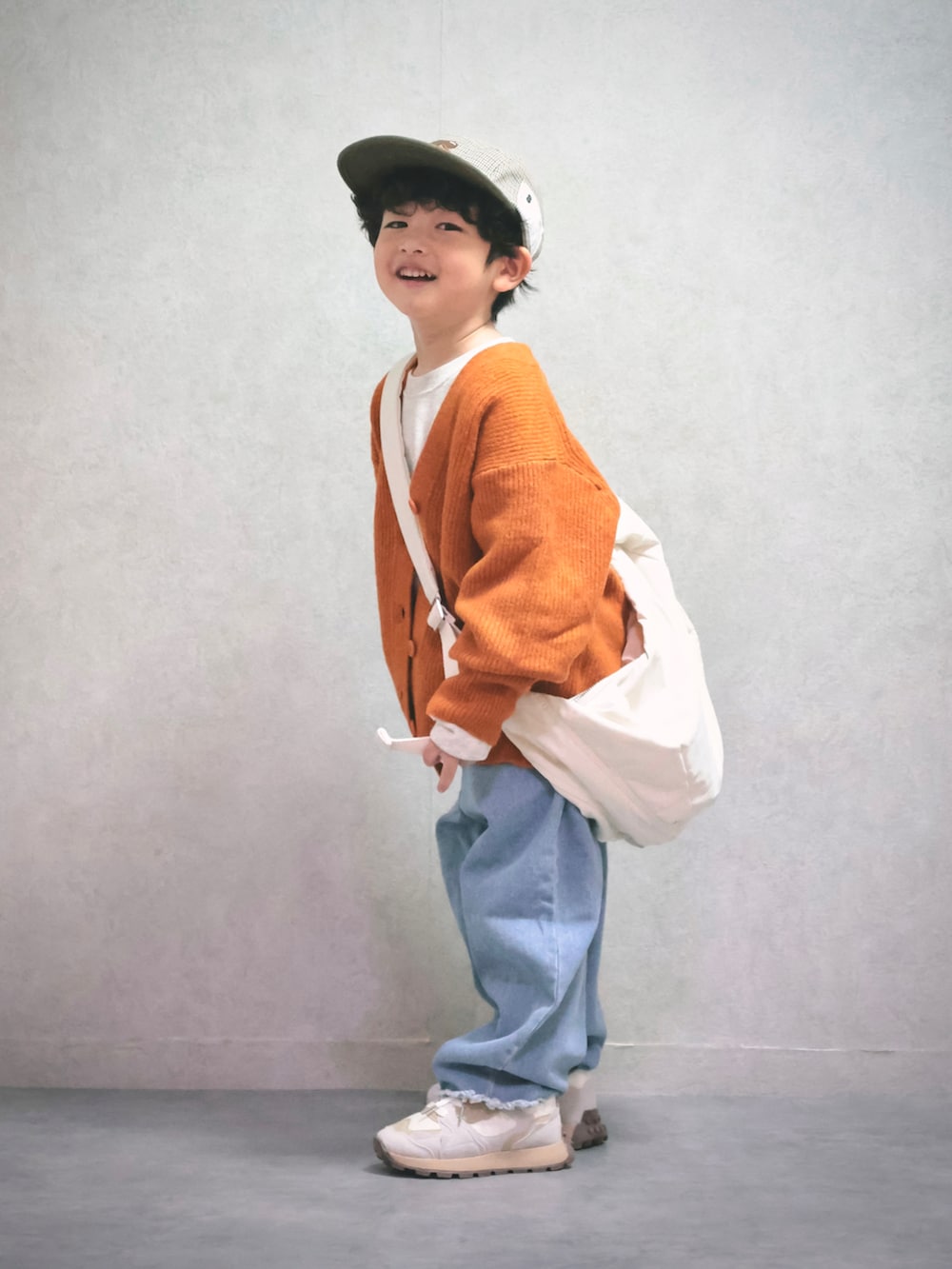 オレンジ系のニット/セーター、ホワイト系のスウェット、ブルー系のデニムパンツを着用したキッズの秋コーディネートの2枚目の写真