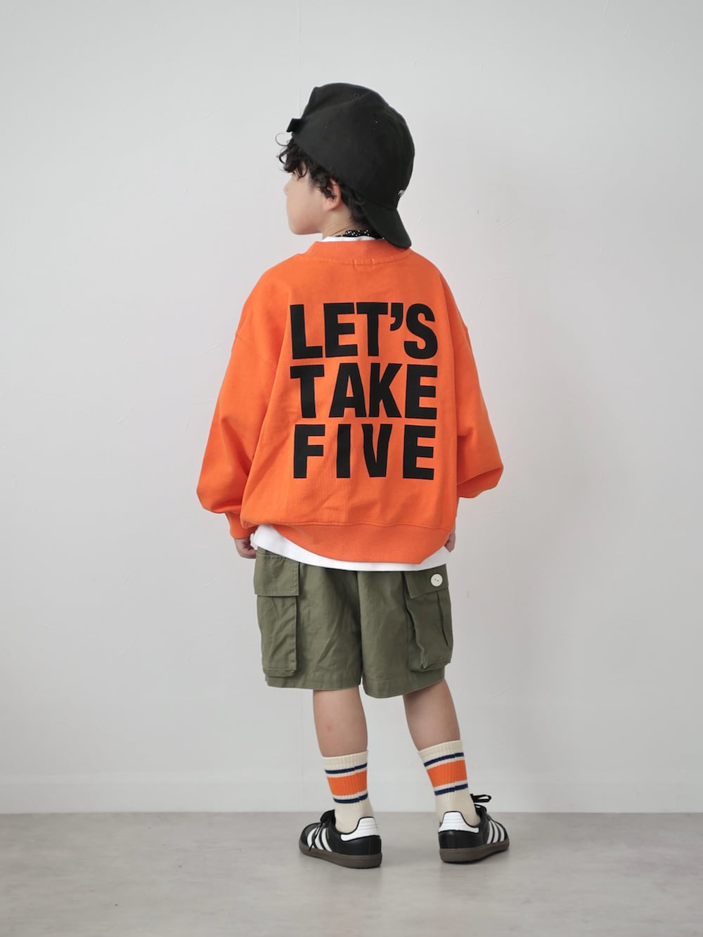 オレンジ系のスウェット、ブラック系のトップス、グリーン系のカーゴパンツを着用したキッズの秋コーディネートの2枚目の写真