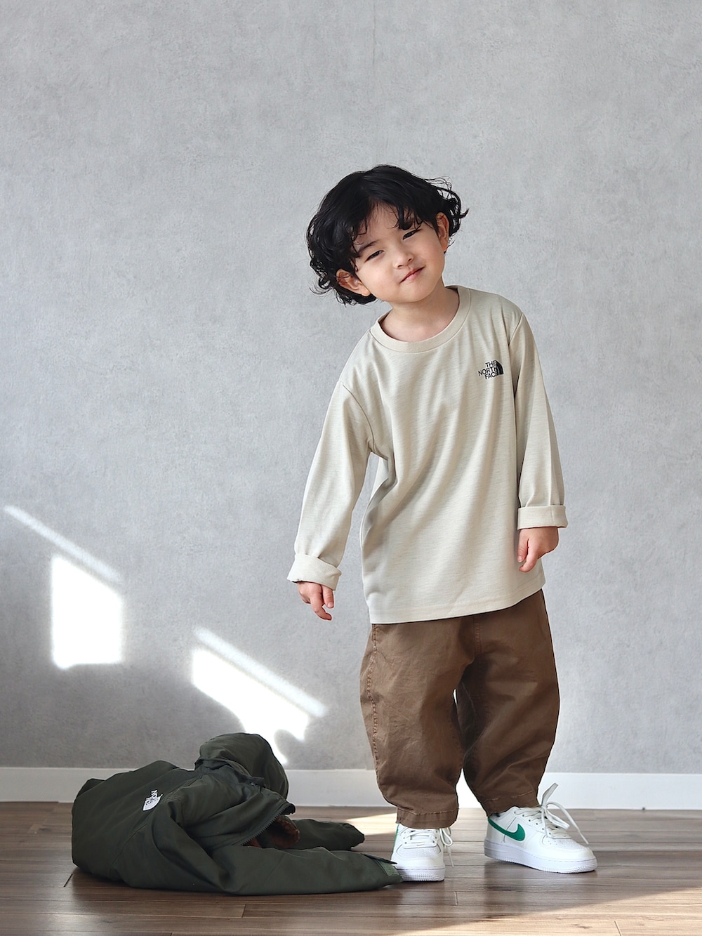 グリーン系のブルゾン、ベージュ系のTシャツ/カットソー、ブラウン系のチノパンツを着用したキッズの冬コーディネートの3枚目の写真