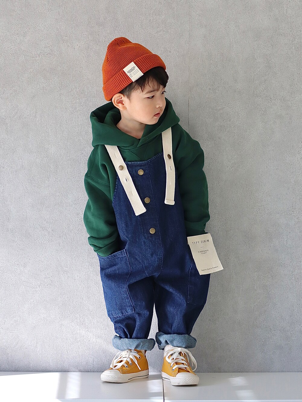 グリーン系のパーカー、ブルー系のサロペット/オーバーオール、イエロー系のスニーカーを着用したキッズの秋コーディネートの2枚目の写真