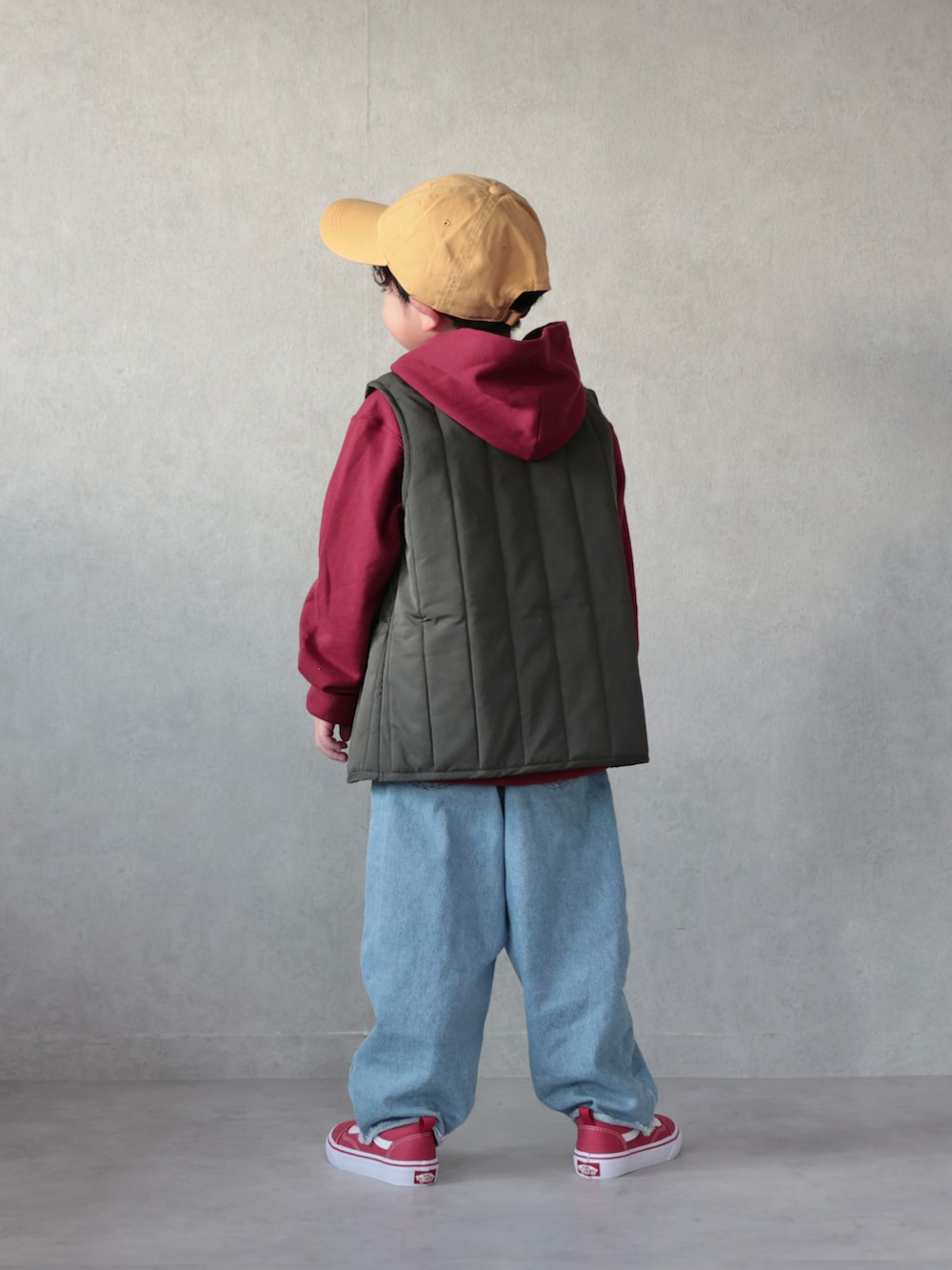 グリーン系のベスト、レッド系のパーカー、ブルー系のデニムパンツを着用したキッズの冬コーディネートの3枚目の写真