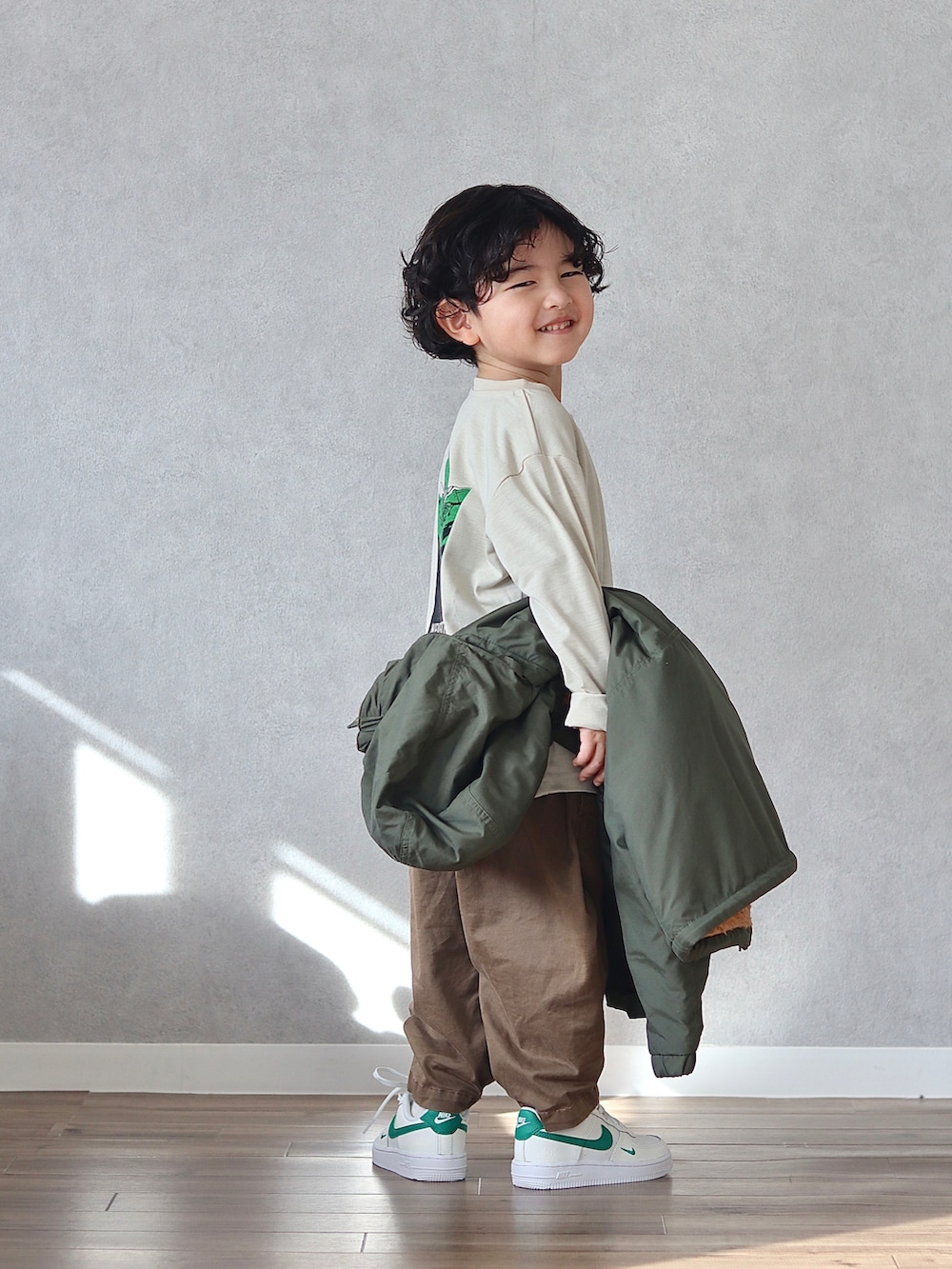 グリーン系のブルゾン、ベージュ系のTシャツ/カットソー、ブラウン系のチノパンツを着用したキッズの冬コーディネートの2枚目の写真
