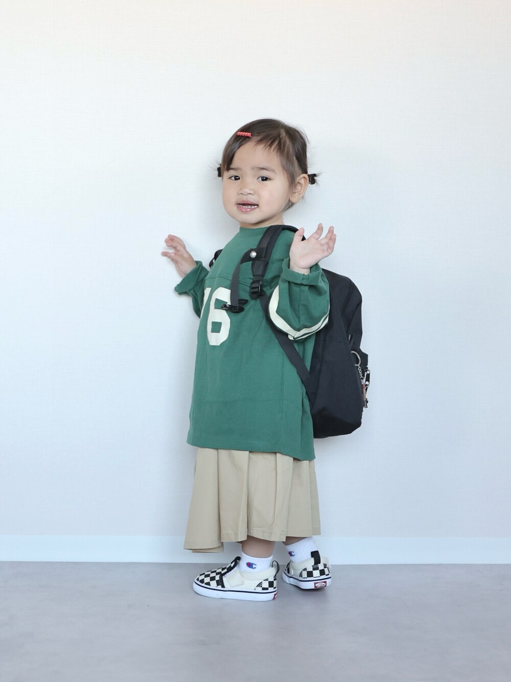 グリーン系のTシャツ/カットソー、ベージュ系のジャンパースカート、ブラック系のスニーカーを着用したキッズの春コーディネートの3枚目の写真