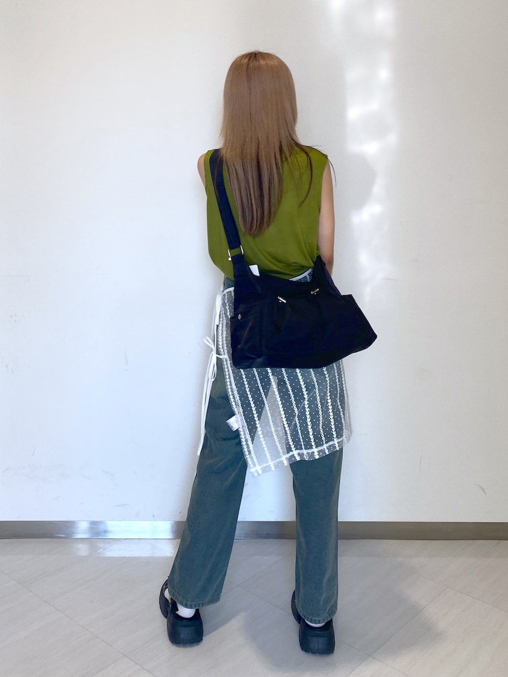 ブルー系のデニムパンツ、ブラック系のショルダーバッグ、グリーン系のタンクトップを着用したレディースの夏コーディネートの4枚目の写真