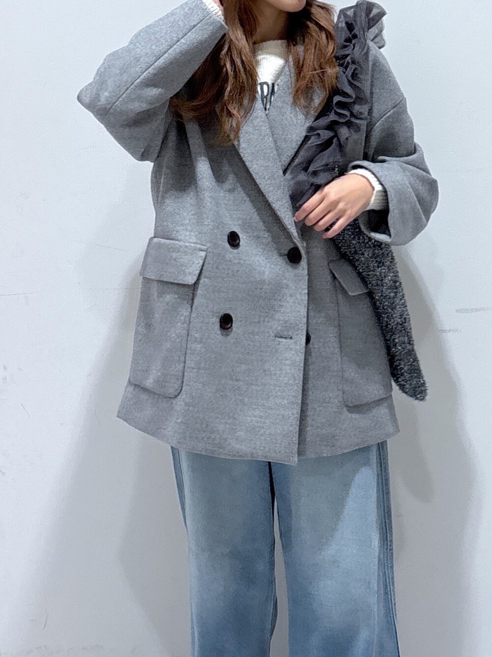 グレー系のピーコート、ホワイト系のニット/セーター、ブルー系のデニムパンツを着用したレディースの冬コーディネートの2枚目の写真