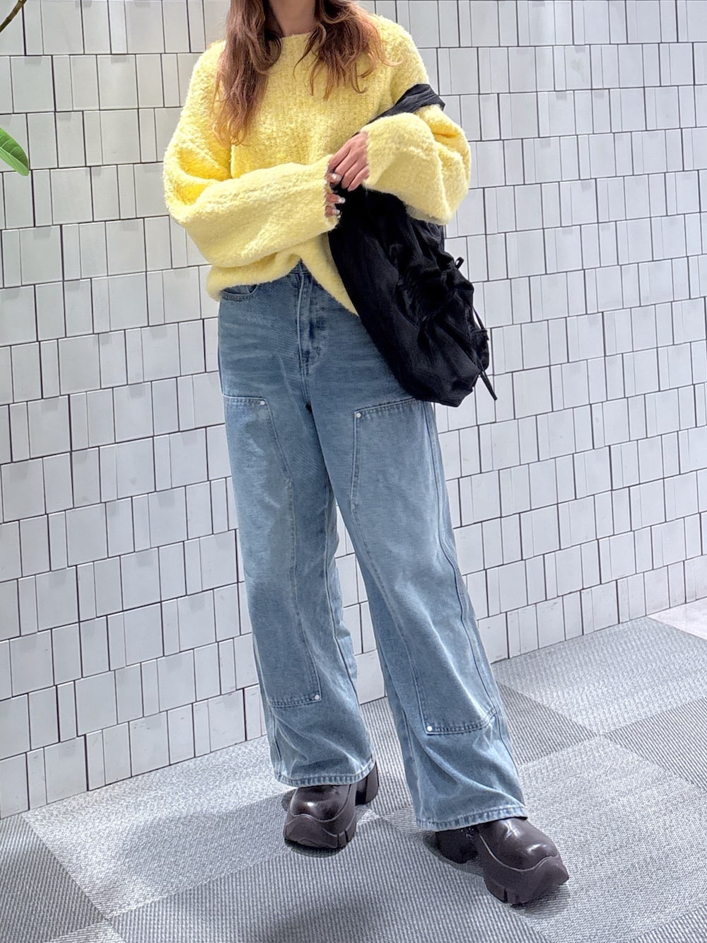 イエロー系のニット/セーター、ブルー系のデニムパンツ、ブラック系のトートバッグを着用したレディースの冬コーディネートの2枚目の写真