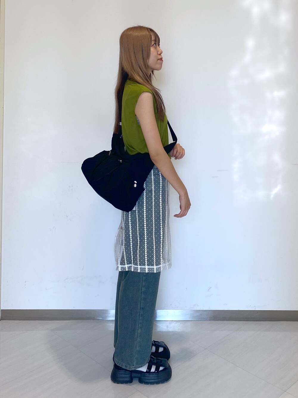 ブルー系のデニムパンツ、ブラック系のショルダーバッグ、グリーン系のタンクトップを着用したレディースの夏コーディネートの2枚目の写真