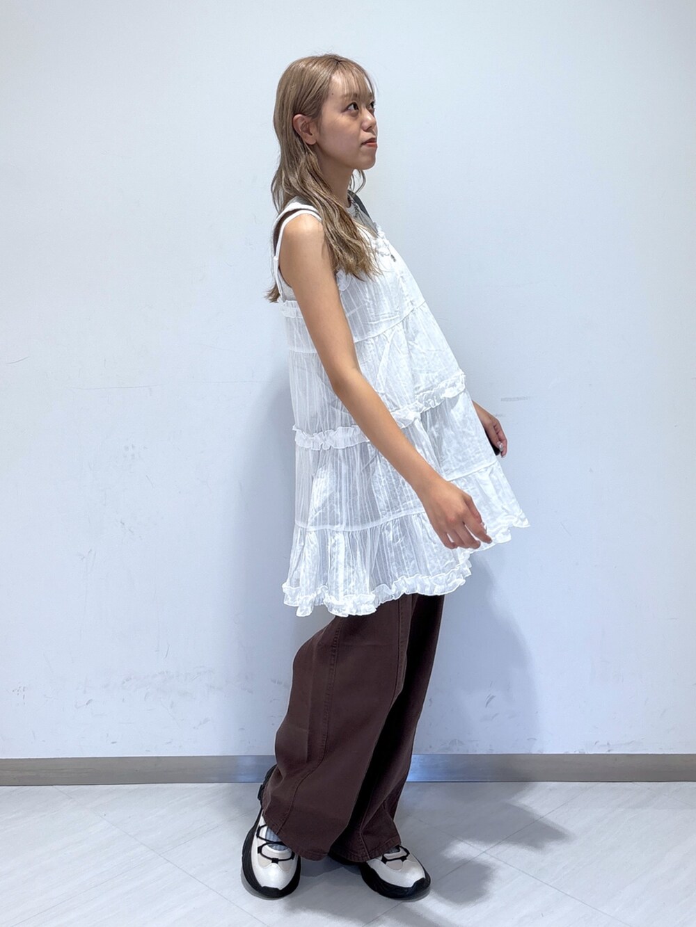 ブラウン系のデニムパンツ、ホワイト系のワンピース、ホワイト系のスニーカーを着用したレディースの夏コーディネートの2枚目の写真