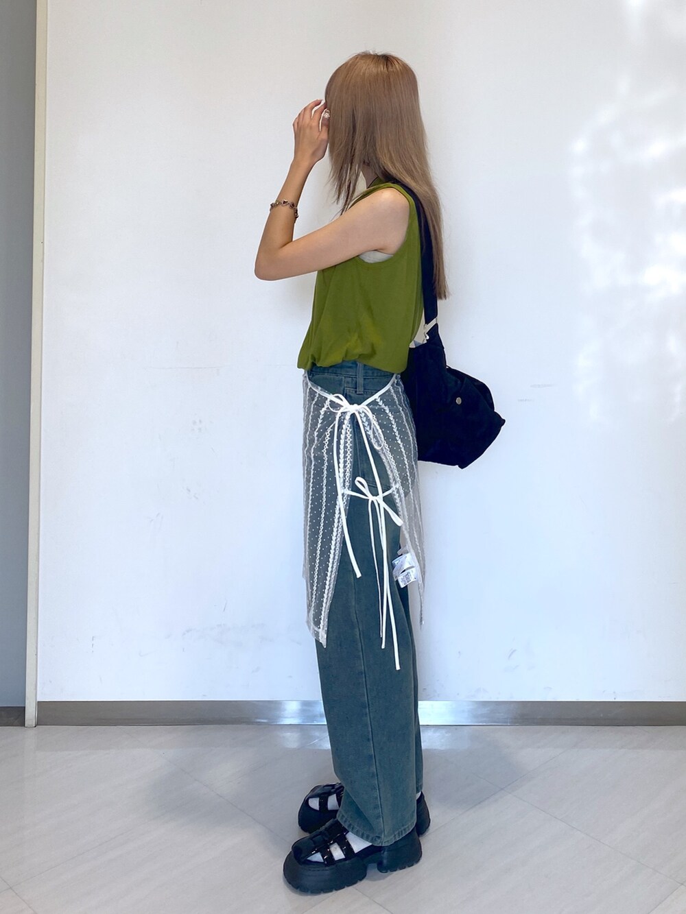ブルー系のデニムパンツ、ブラック系のショルダーバッグ、グリーン系のタンクトップを着用したレディースの夏コーディネートの3枚目の写真