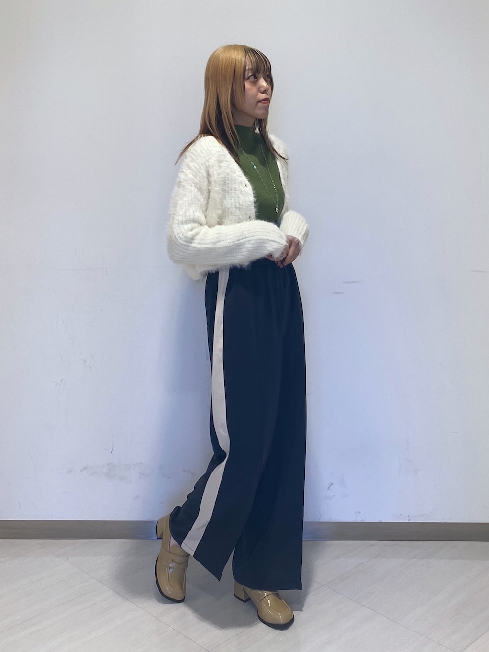 グレー系のその他パンツ、ベージュ系のローファー、グリーン系のニット/セーターを着用したレディースの冬コーディネートの2枚目の写真