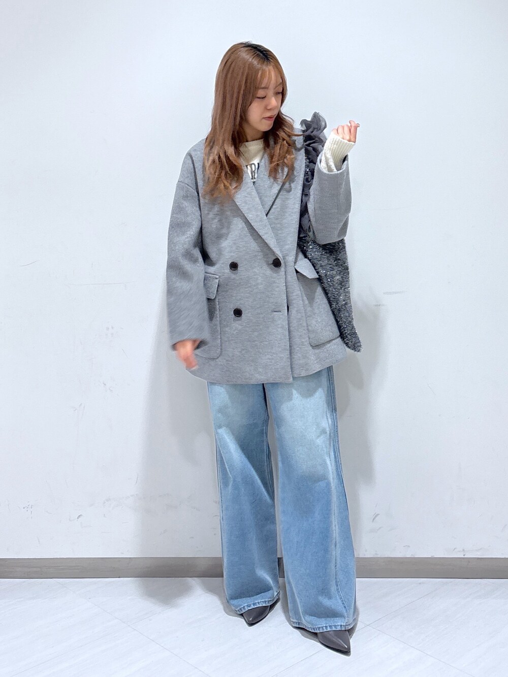 グレー系のピーコート、ホワイト系のニット/セーター、ブルー系のデニムパンツを着用したレディースの冬コーディネートの3枚目の写真