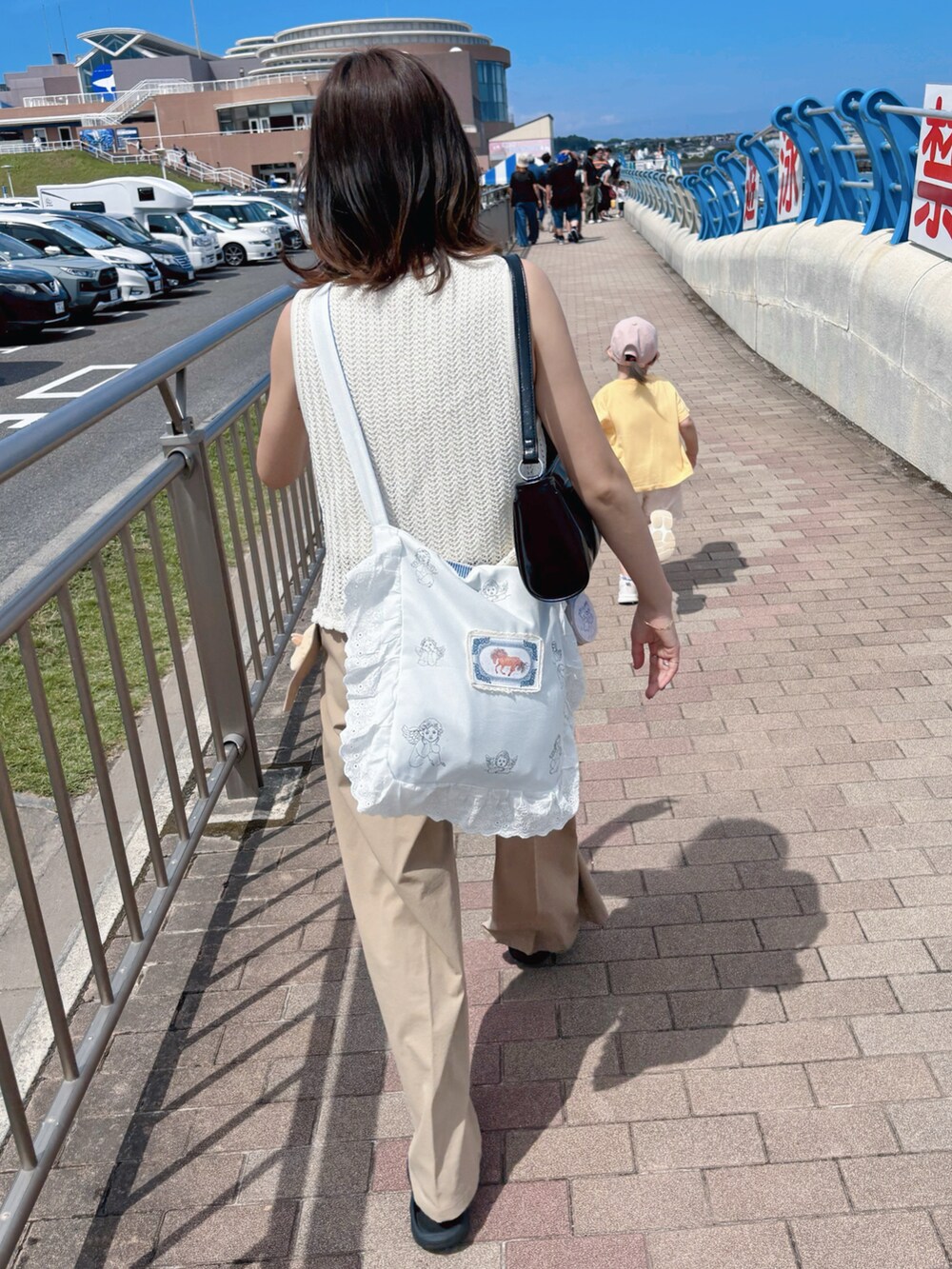ホワイト系のベスト、ベージュ系のパンツ、ブラック系のショルダーバッグを着用したレディースの夏コーディネートの2枚目の写真